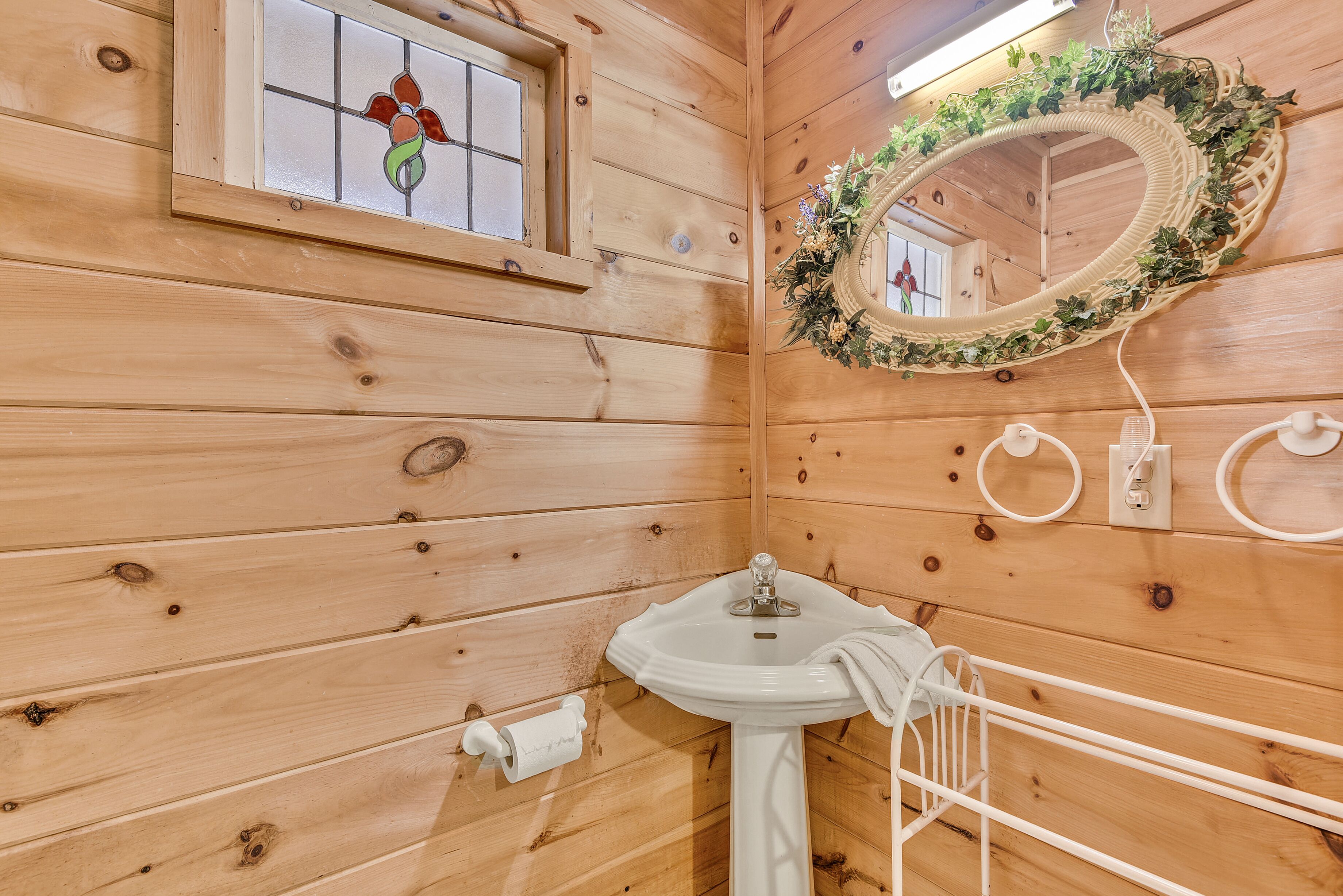 A wooden cabin bathroom with a sink, mirror, and window.