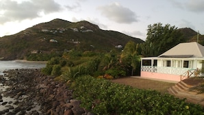 A coastal property with a rocky shoreline, lush greenery, and a house with a white exterior and a grey roof. - Luxurious Oceanfront Villa with Stunning Views Over Montserrat (Falmouth Harbour)