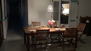 A dining area with a wooden table and chairs, a hanging light fixture, and a door with a cross symbol. - Luxurious Oceanfront Villa with Stunning Views Over Montserrat (Falmouth Harbour)