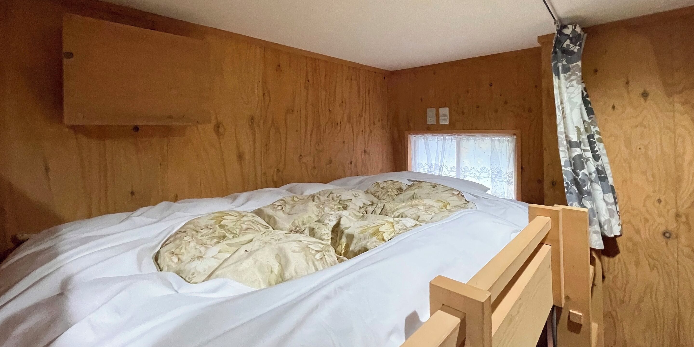 A wooden room with a bed, a window with a curtain, and a wooden headboard.