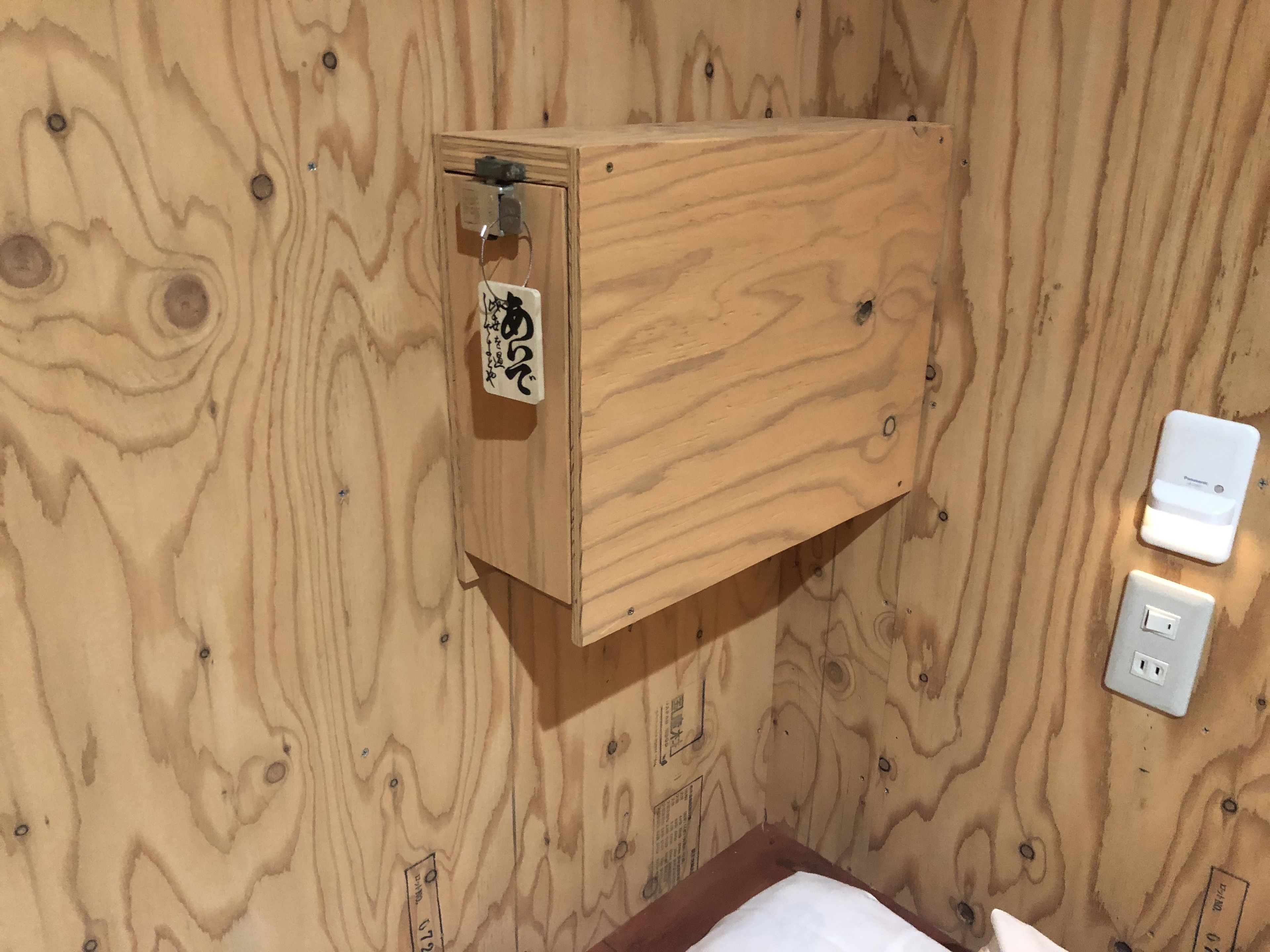 Een houten kastje met een slot en sleutelgat, bevestigd aan een muur met zichtbare stopcontacten.