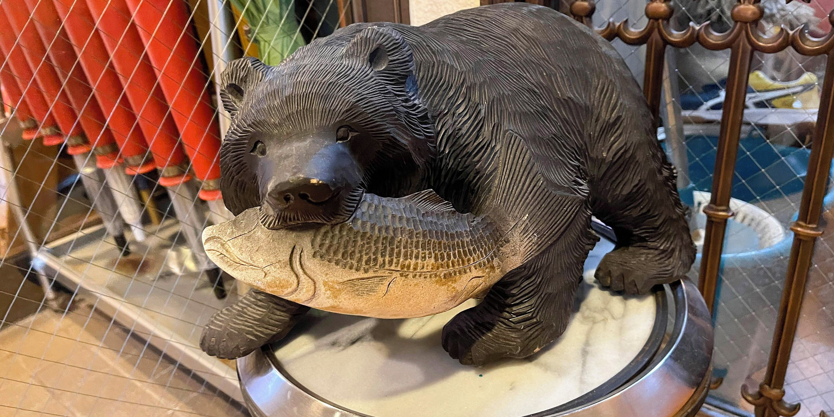 A bear statue holding a fish, placed on a circular platform with a metal railing.