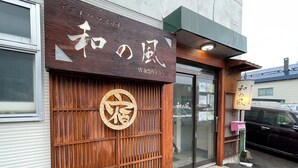 A building with a wooden facade and a large circular emblem. - Guest House Otaru WANOKAZE - Hostel (Otaru)