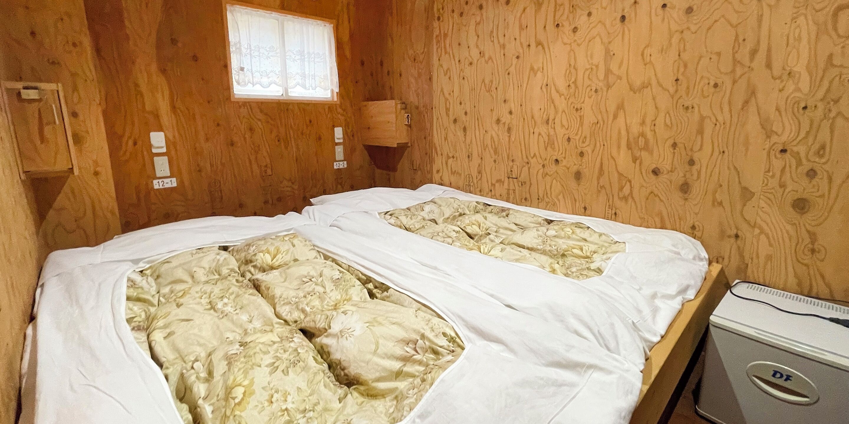 A wooden cabin room with two beds, a window, and a small wooden cabinet.