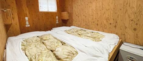 A wooden cabin room with two beds, a window, and a small wooden cabinet.