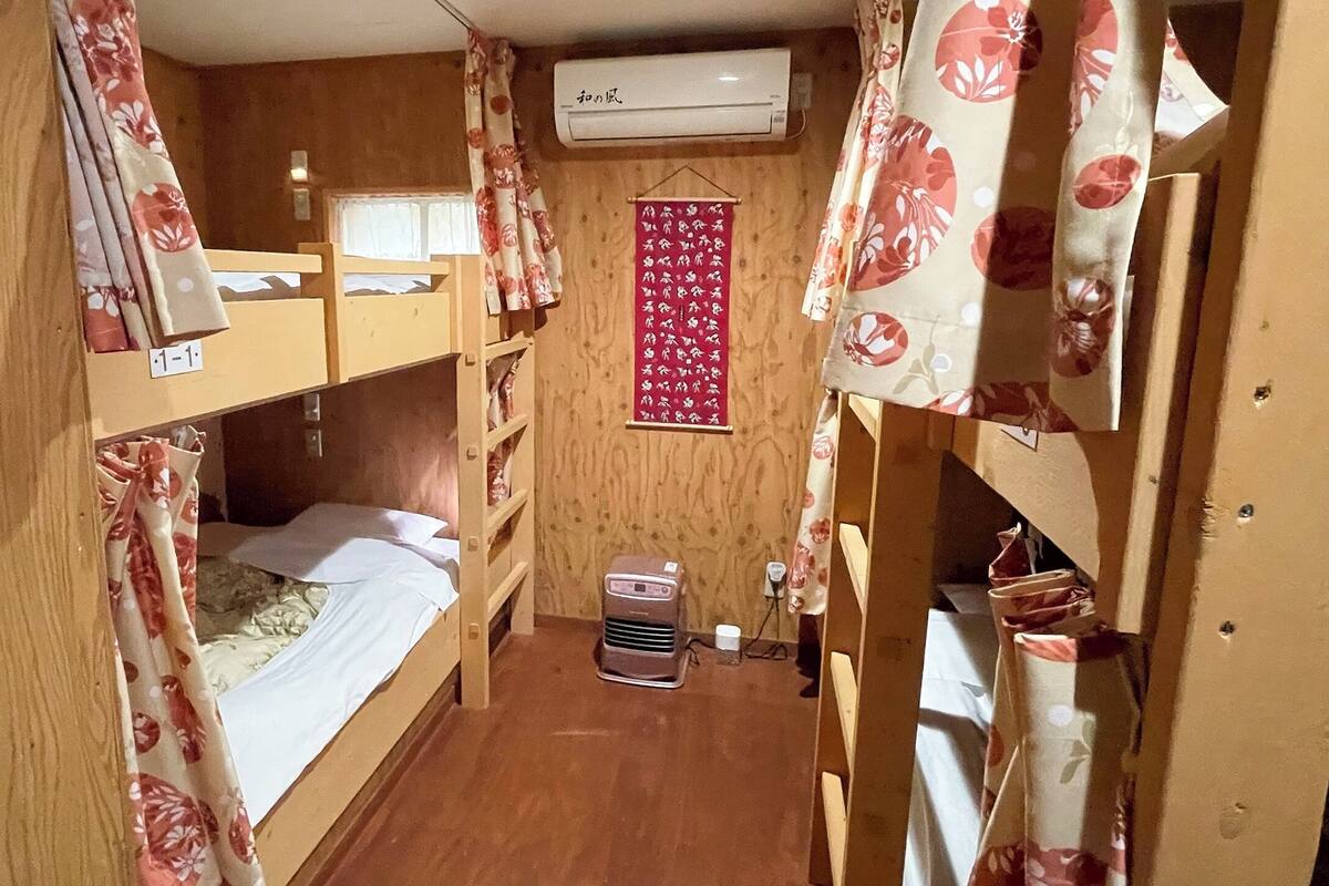 A narrow room with wooden bunk beds, a small heater, and a red decorative item on the wall.