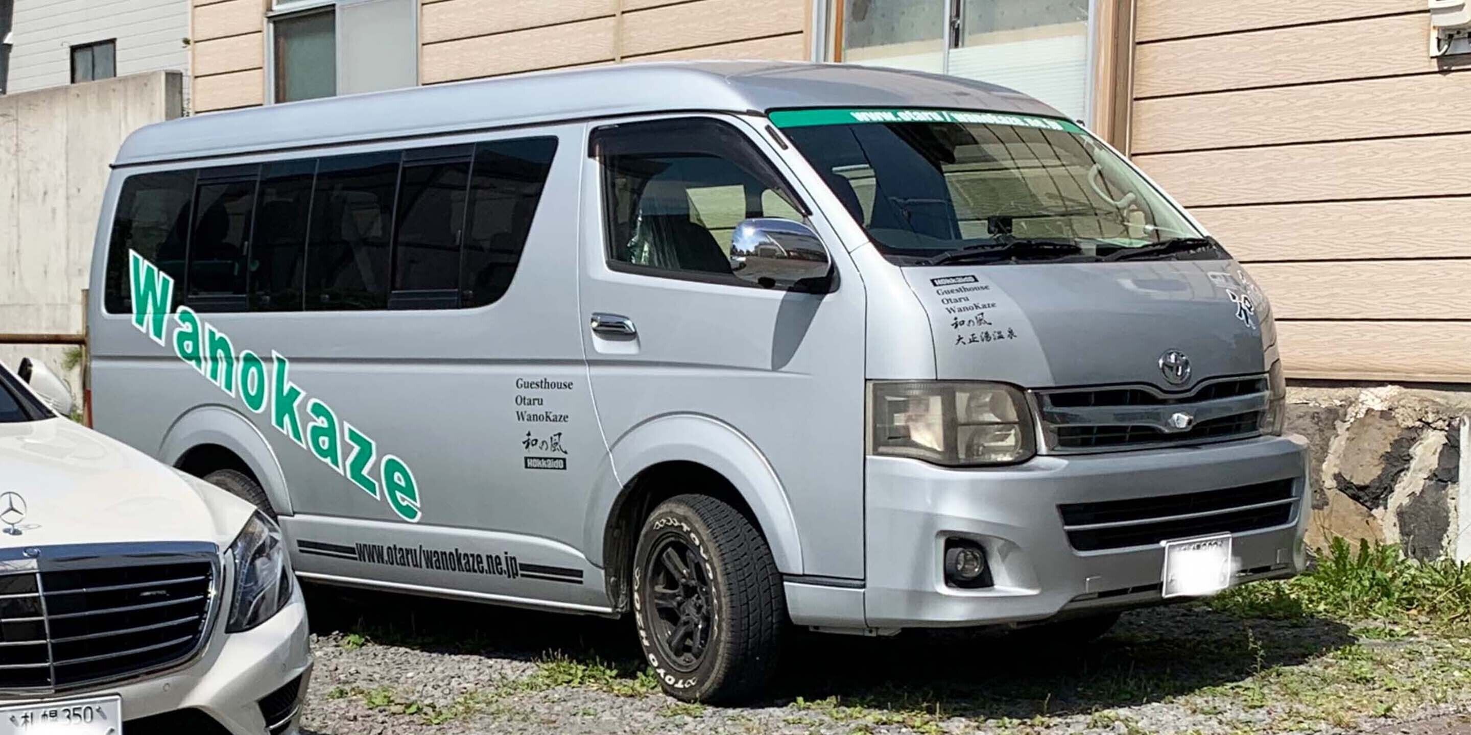 Un furgone argentato con la scritta "WanoKaze" parcheggiato di fronte a un edificio.