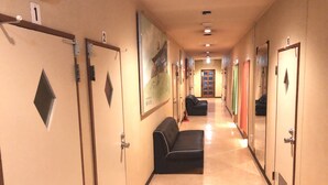 A hotel hallway with doors numbered 1 to 6, a black leather sofa, and a fire extinguisher. - Guest House Otaru WANOKAZE - Hostel (Otaru)