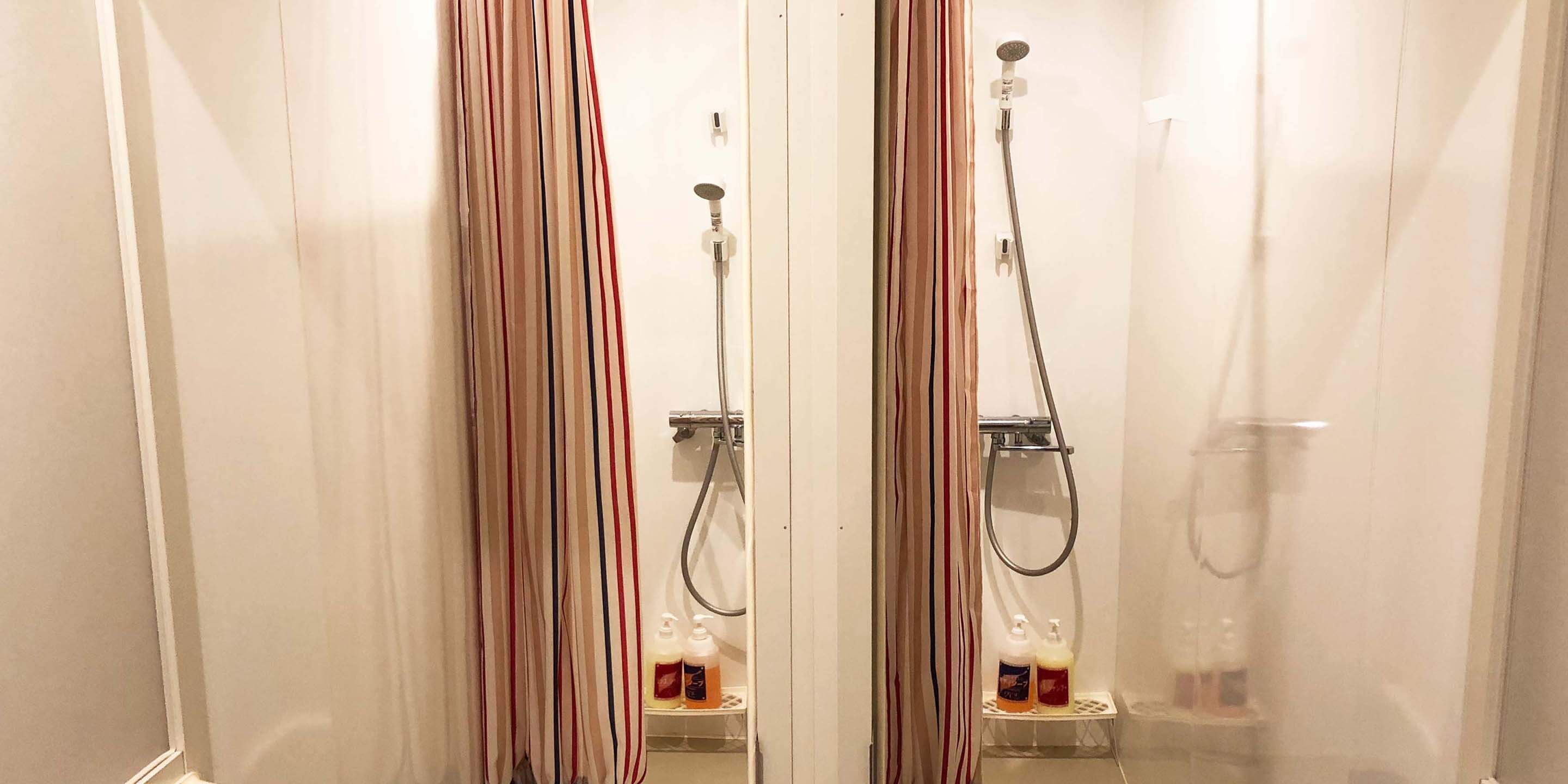 Un baño con dos cabinas de ducha, cada una con un cabezal de ducha de mano y zona de ducha con mampara de vidrio. Hay dos botellas de jabón en una repisa dentro de cada cabina.