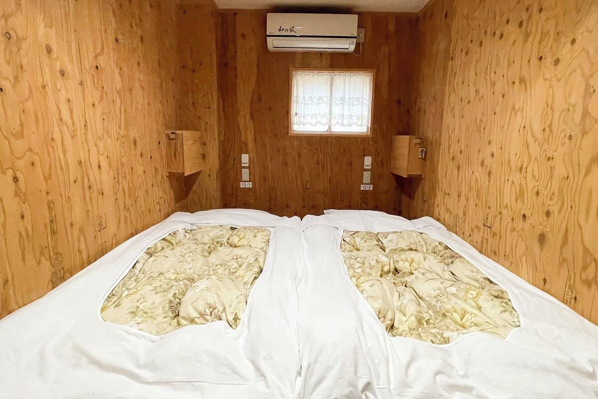 A wooden-paneled room with a bed, an air conditioning unit, and a window with curtains.
