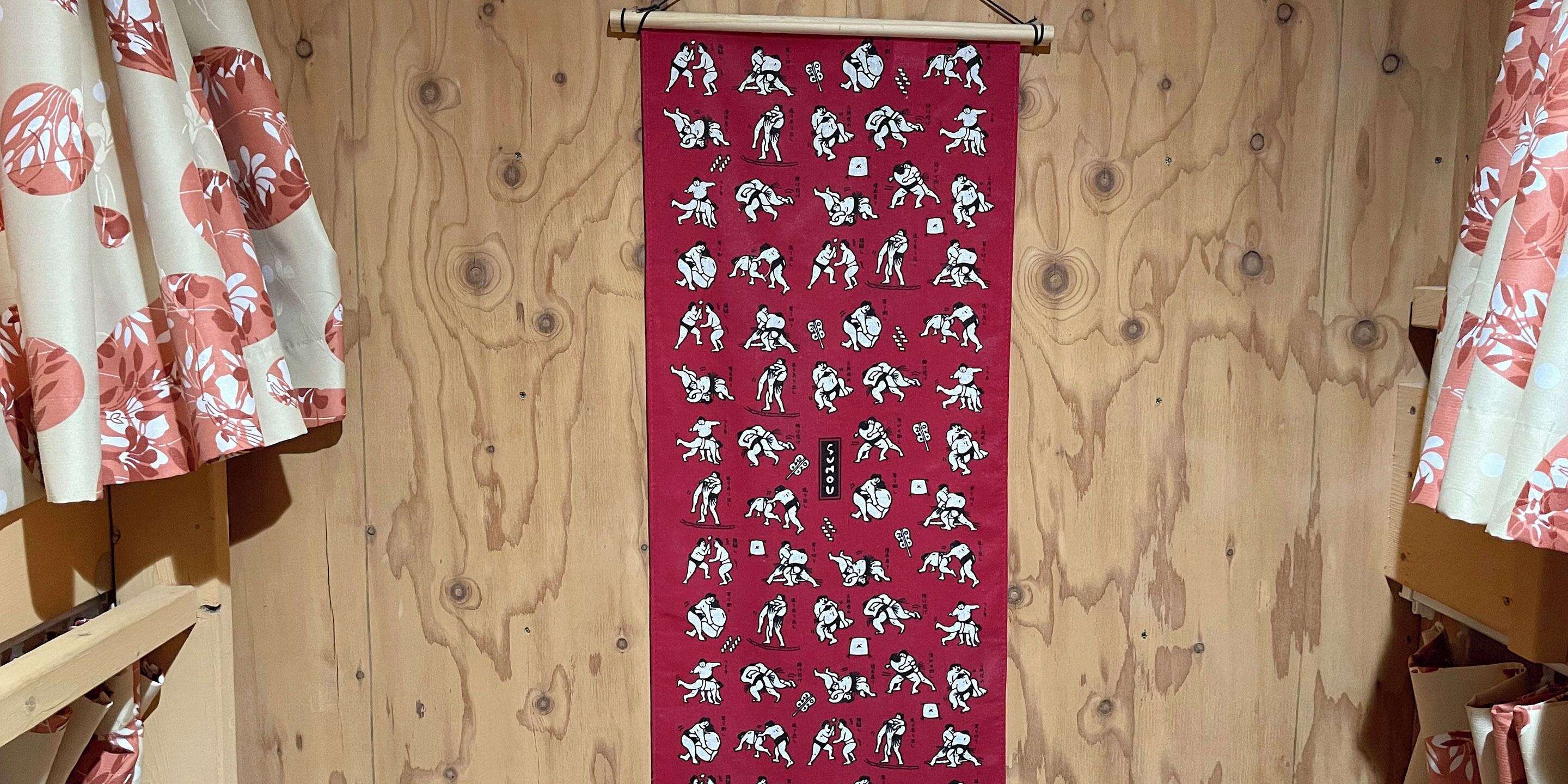 Pared de madera con un estandarte rojo que muestra ilustraciones de lucha libre sumo.