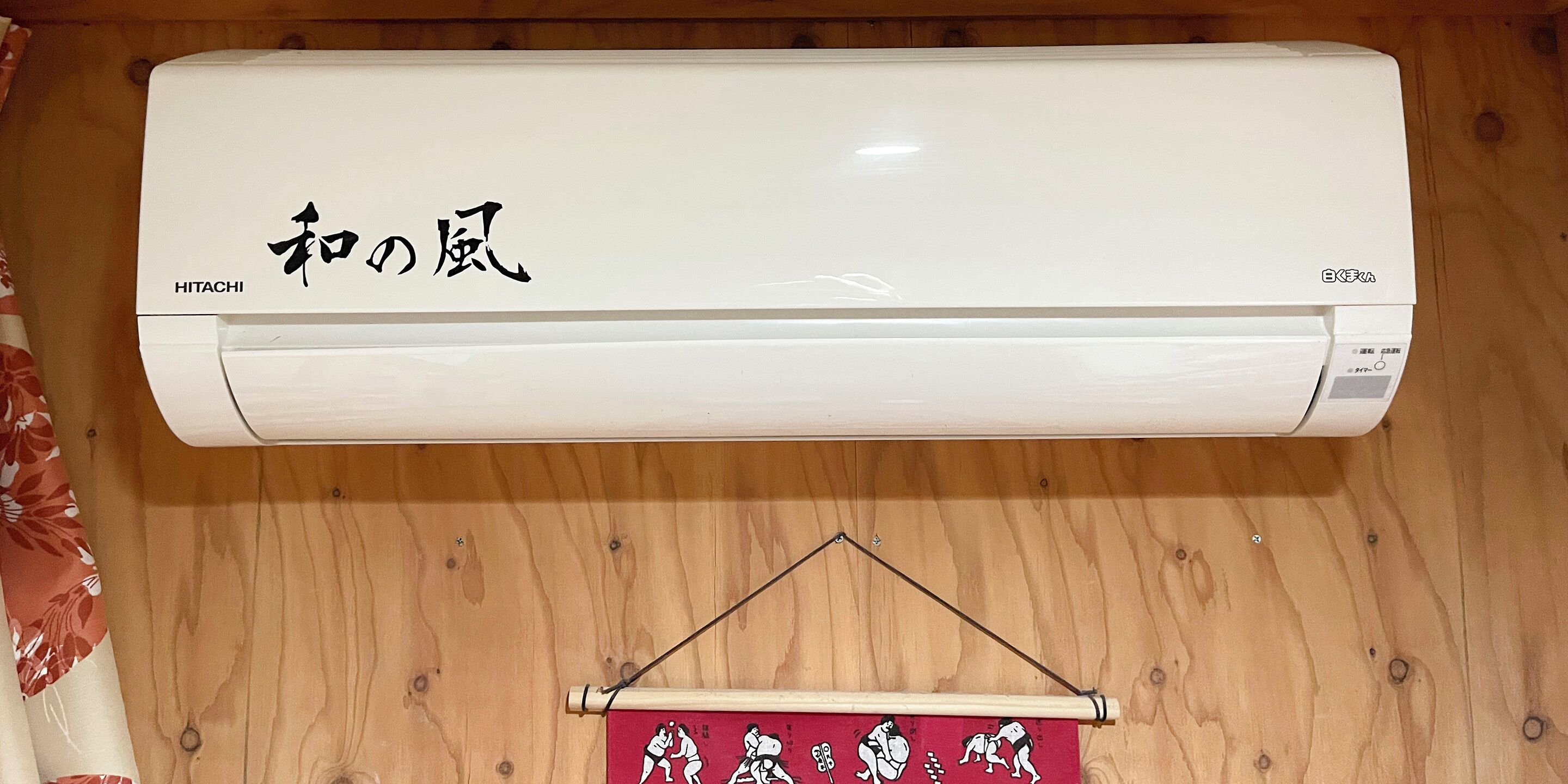 A white air conditioner mounted on a wooden wall with Japanese characters and the brand name "HITACHI".