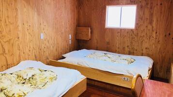 A small, wooden room with two single beds, a window, and an air conditioning unit.
