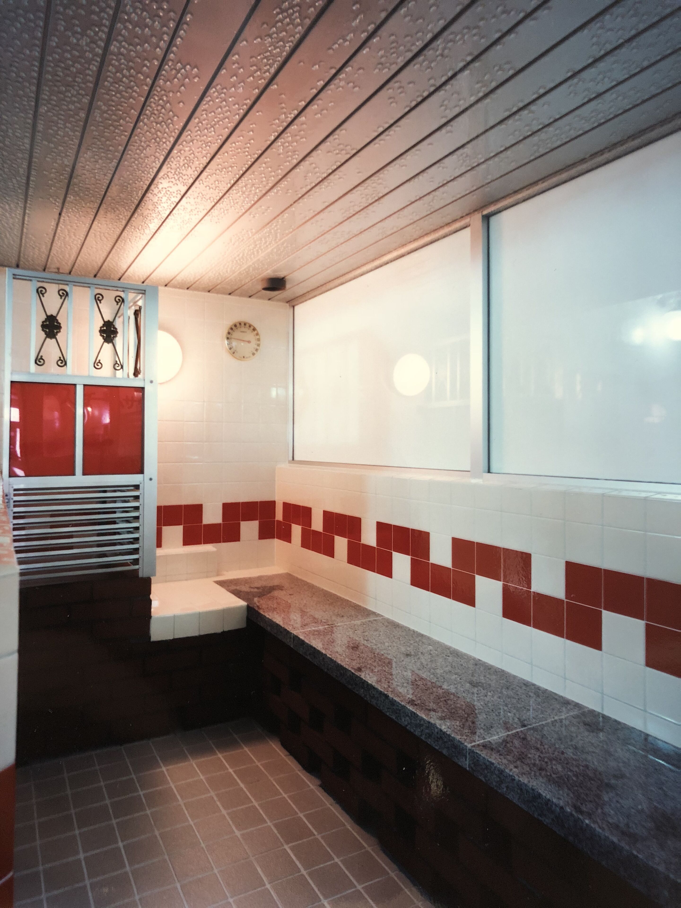 A bathroom with a tiled wall, a clock, and a window.