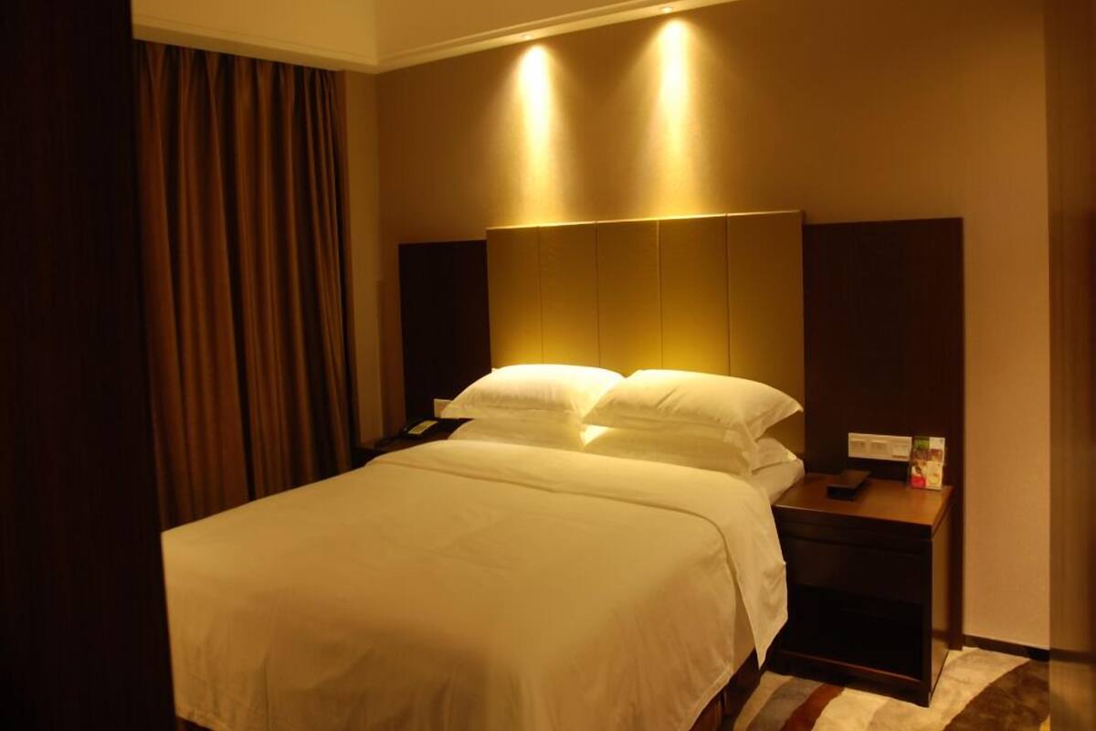 A hotel room with a large bed, two bedside tables, a nightstand, and a headboard with integrated lighting.