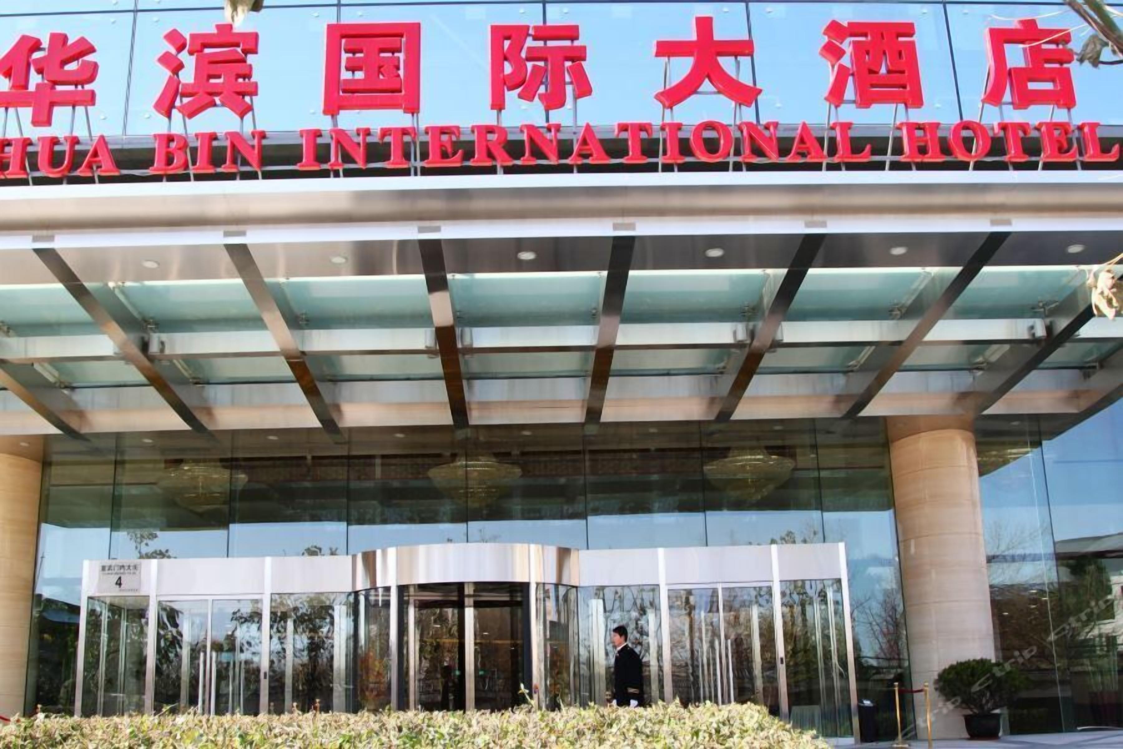 L’entrée de l’hôtel international Hua Bin, avec sa façade moderne en verre et un ciel dégagé au-dessus.