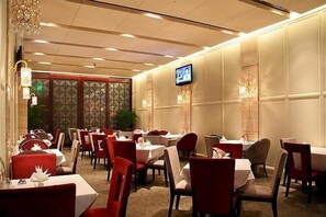 A restaurant with multiple tables and chairs, a television screen, and decorative lighting.