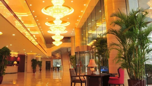 Eine geräumige Lobby mit einem modernen Kronleuchter, einer Rezeption und einer Sitzecke mit Tisch und Stühlen.