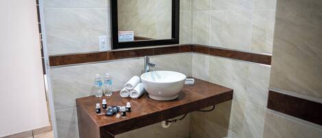 Un baño con lavamanos blanco, espejo y encimera marrón. Hay artículos de aseo en la encimera.