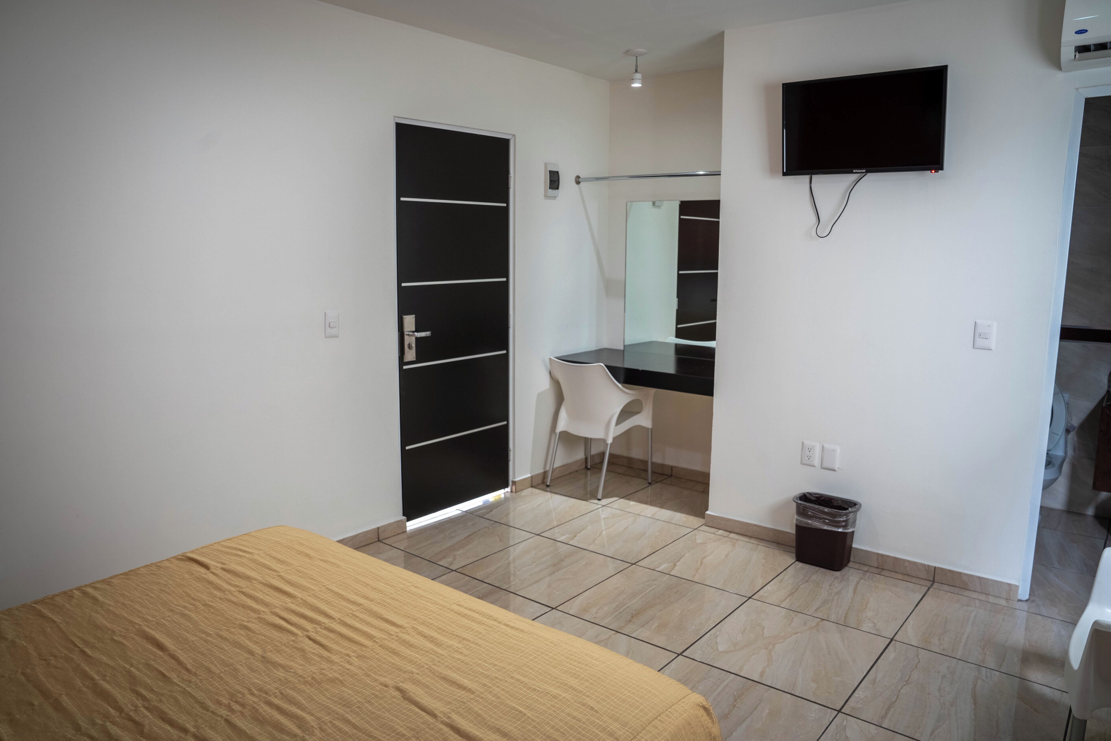 Una camera da letto con un letto, una scrivania, una sedia, una TV e un cestino.
