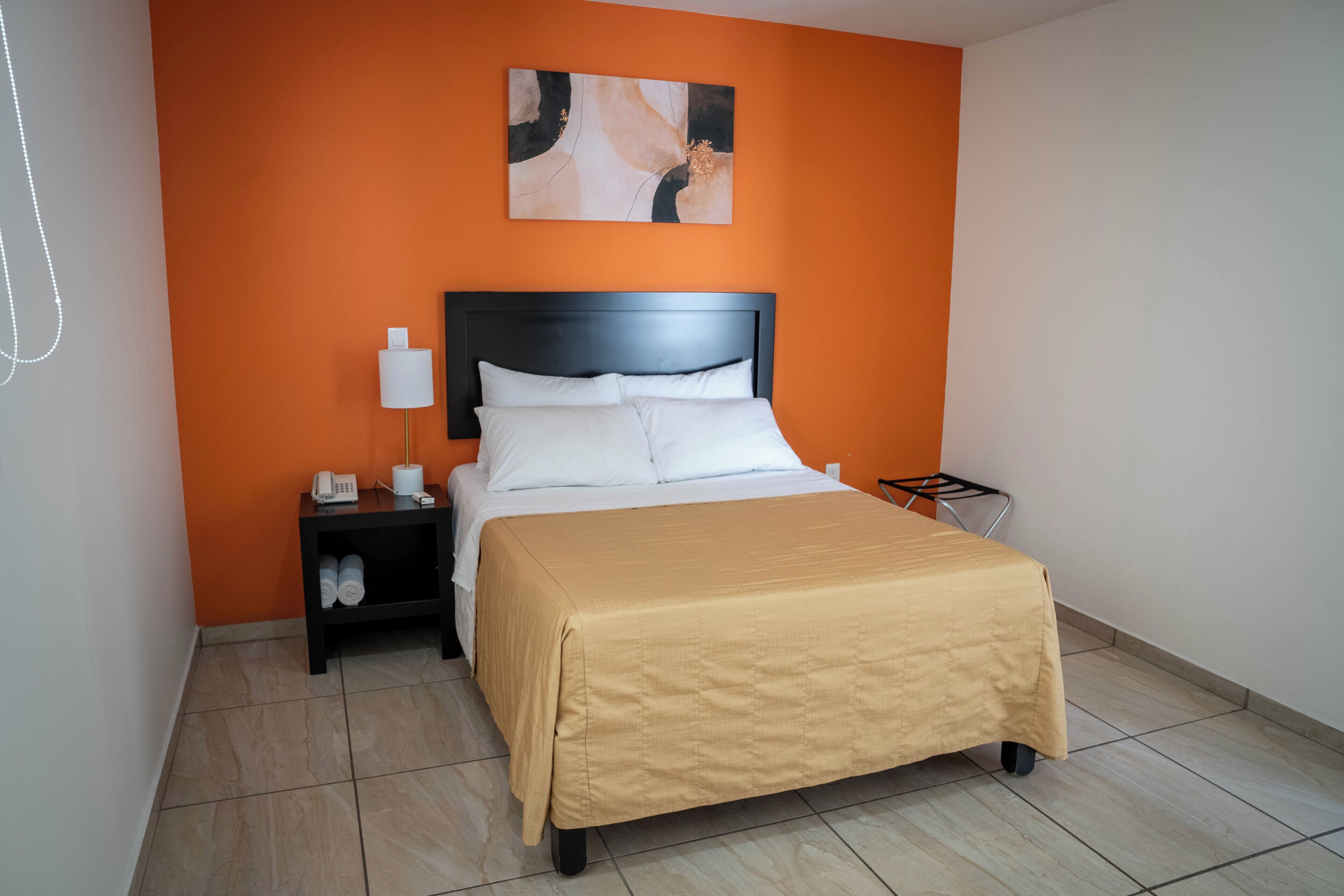 A hotel room with a bed, a nightstand, a lamp, and a wall-mounted artwork.