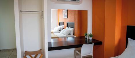 Una habitación de hotel moderna con una cama, un escritorio, una silla, una mesita, un aire acondicionado y un espejo.