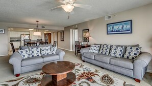 A living room with two grey sofas, a wooden coffee table, a ceiling fan, and a framed painting of sailboats. - Upscale Waterway View Condo, Onsite Golf Course | Yacht Club Villas - 3-303 (North Myrtle Beach)