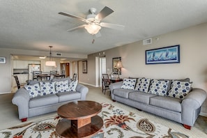 A living room with two grey sofas, a wooden coffee table, a ceiling fan, and a framed painting of sailboats. - Upscale Waterway View Condo, Onsite Golf Course | Yacht Club Villas - 3-303 (North Myrtle Beach)