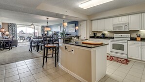 A modern kitchen with white cabinets, a central island, and a dining area with chairs and a table. - Upscale Waterway View Condo, Onsite Golf Course | Yacht Club Villas - 3-303 (North Myrtle Beach)