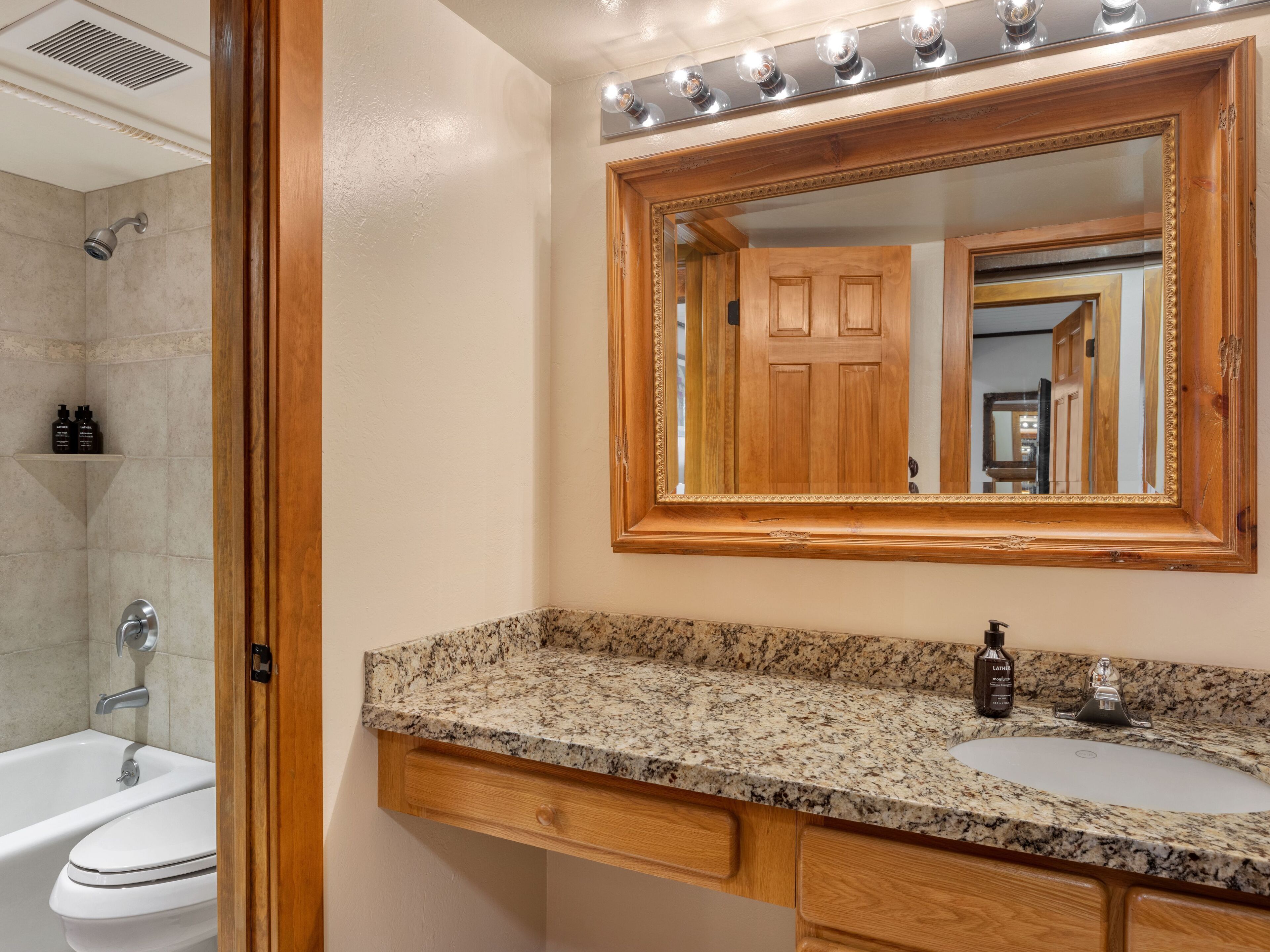 A bathroom with a granite countertop, a sink, a mirror, and a shower.