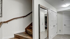 Un escalier avec des marches en bois et une rampe, menant à une pièce aux murs blancs et dotée d’un grand miroir qui reflète une porte et un placard.