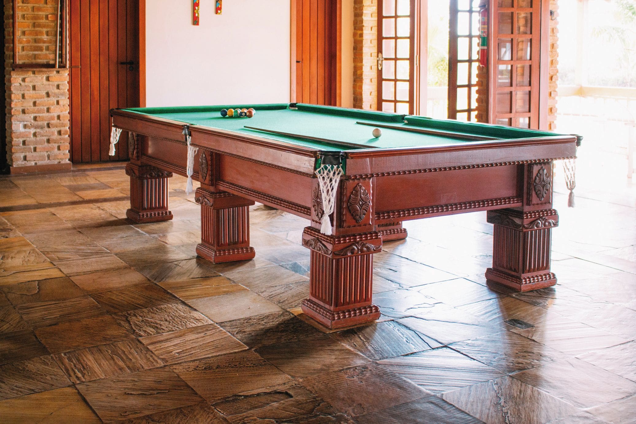 A pool table with a green felt surface, surrounded by wooden flooring and a brick wall.