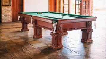 A pool table with a green felt surface, surrounded by wooden flooring and a brick wall.
