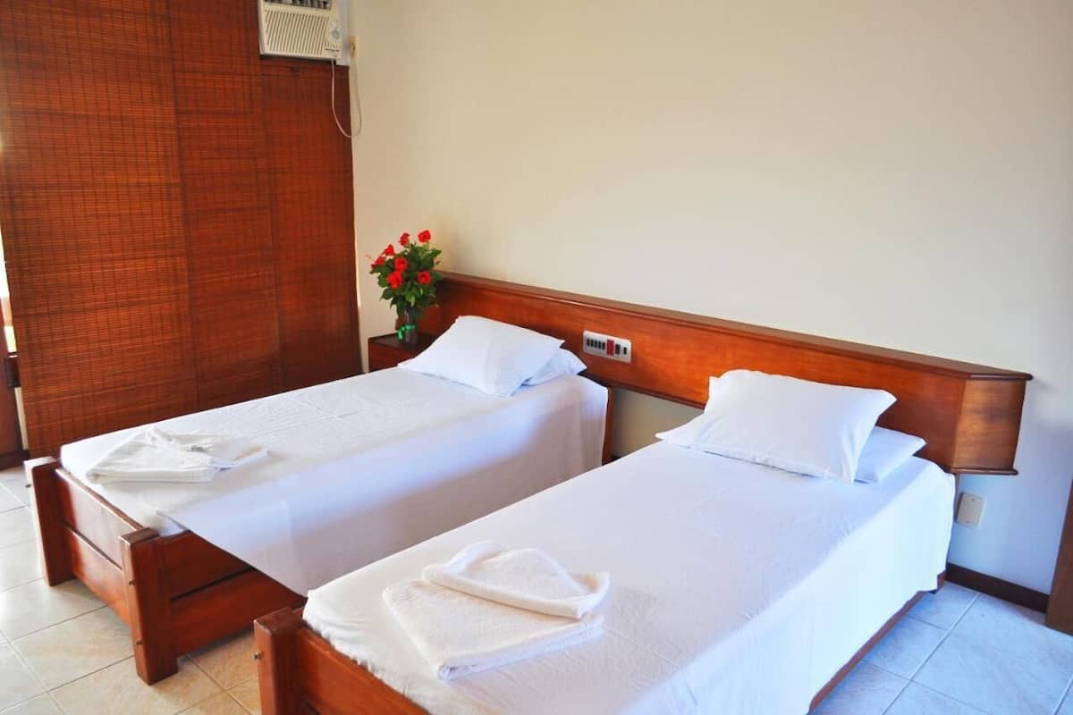 Two single beds with wooden headboards, white linens, and a small bedside table with a vase of red flowers.