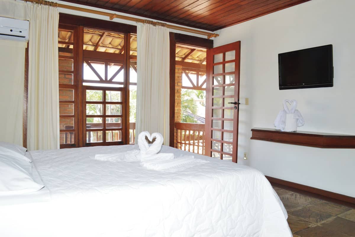 A hotel room with a bed, a TV mounted on the wall, and a view of the outdoors through a wooden door.