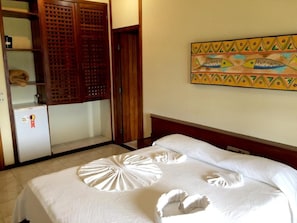 A hotel room with a bed, a wardrobe, a small refrigerator, and a decorative wall piece.