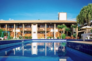 A hotel with a swimming pool, multiple balconies, and a clear blue sky.