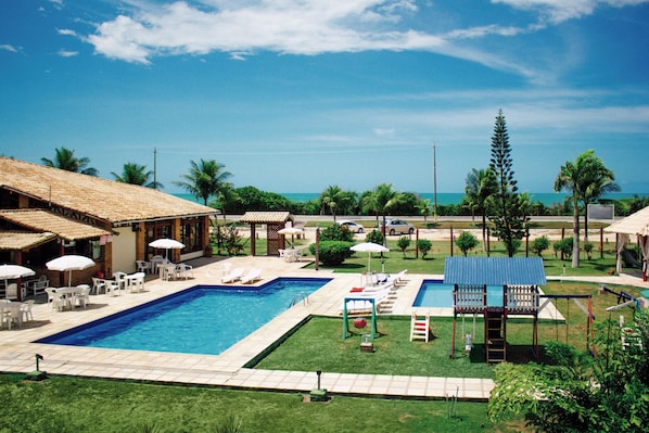 A pool area with two pools, lounge chairs, umbrellas, and a view of the ocean.