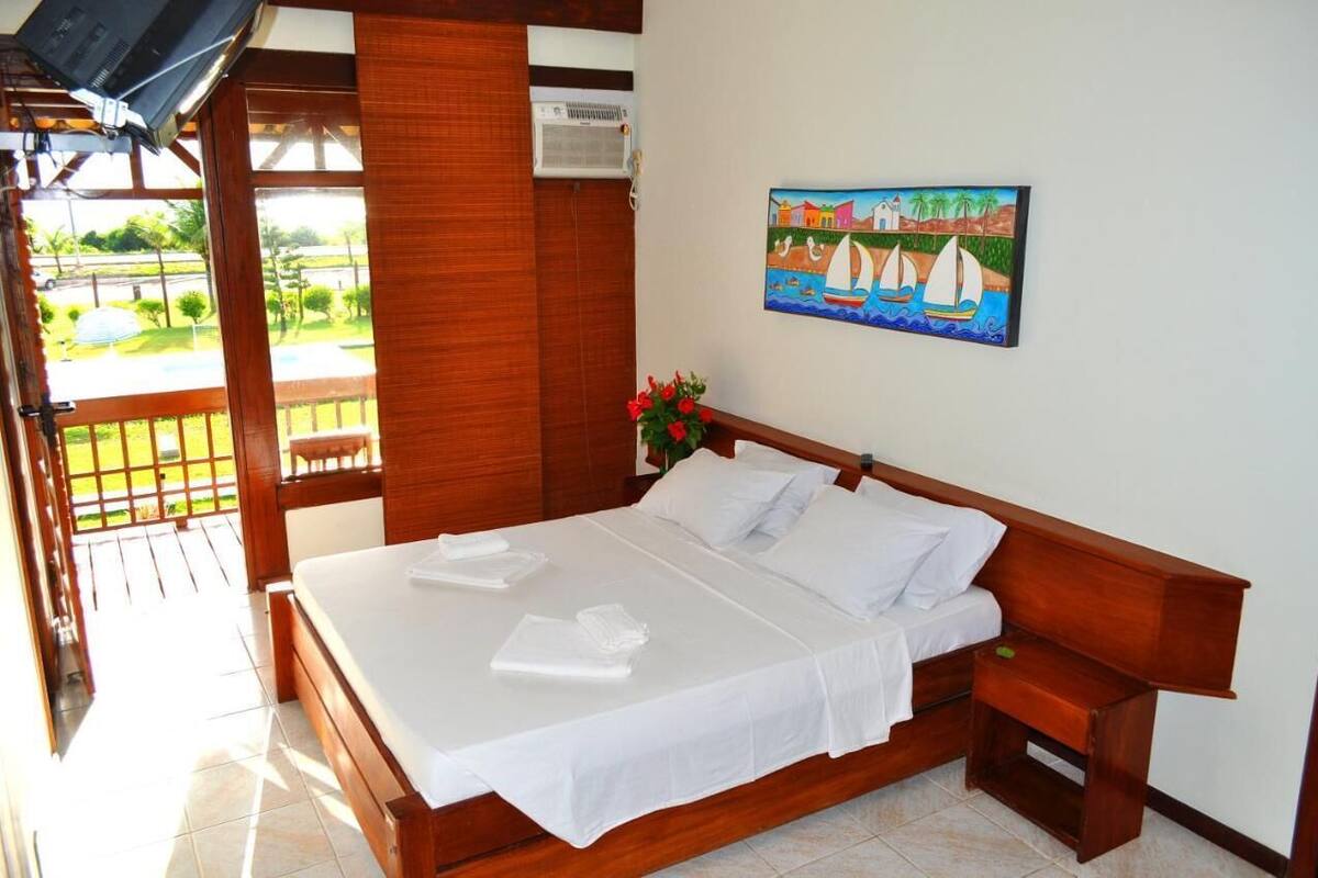A wooden bed with white linens, a painting of sailboats, and a small nightstand with a green object.