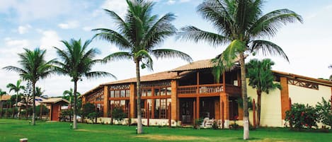 A two-story building with a tiled roof, surrounded by a well-maintained lawn and palm trees.