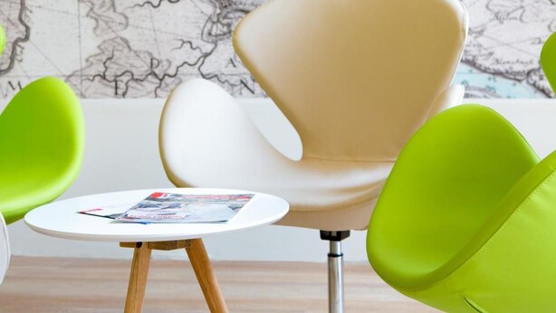 A room with a large map on the wall, a round table with a magazine, and two green chairs. - Hotel Nordraum (Bremen)