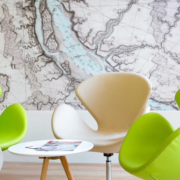 Une pièce avec une grande carte accrochée au mur, une table ronde sur laquelle repose un magazine, et deux chaises vertes.