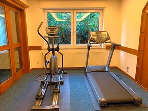 A home gym with an elliptical, a treadmill, and a stationary bike, with a window providing a view of greenery.