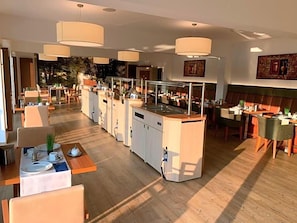 A modern hotel dining area with multiple tables, pendant lighting, and a view of the outdoors.