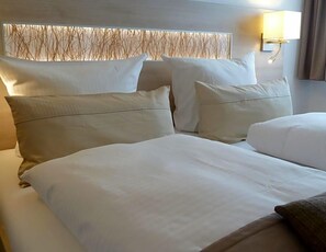 A hotel room with a large bed, multiple pillows, a headboard with a textured design, and a wall-mounted light fixture.