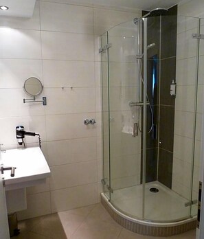 A bathroom with a glass-enclosed shower, a sink with a hairdryer, and a mirror on the wall. - Hotel Restaurant Goldenstedt (Delmenhorst)