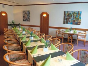 A dining area with multiple tables and chairs, each with a green napkin and a small plant.