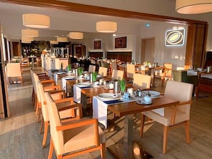 A hotel dining area with multiple tables and chairs, some with table settings.
