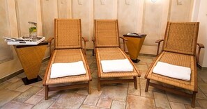Three wicker lounge chairs with white cushions, arranged in a row on a tiled floor.