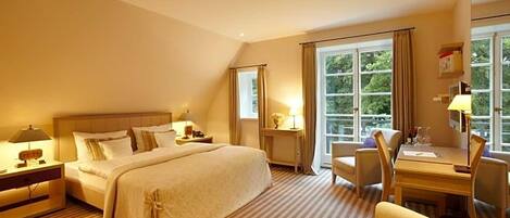 A hotel room with a large bed, a desk with a chair, and a window with curtains.